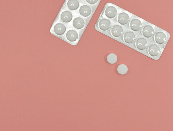 zwei Tablettenblister und zwei einzelne Tabletten auf rosa Untergrund E-rezept