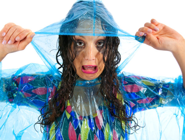 Frau mit blauem Regencape und verschmiertem Make-up durch Regen
