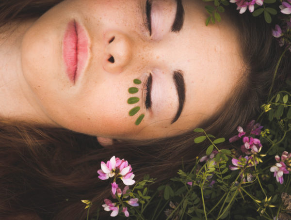 Frau liegt auf einer Wiese mit Blumen, Nahaufnahme von dem Gesicht, Augen sind geschlossen