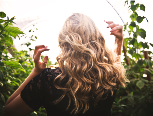 Blondhaarige Frau von hinten fotografiert steht zwischen hohe Pflanzen