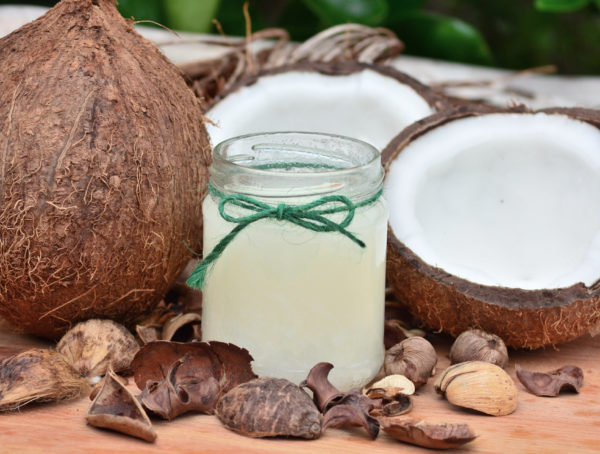 Einwegglas mit Kokosnussöl umgeben von aufgeschlagenen Kokosnüssen