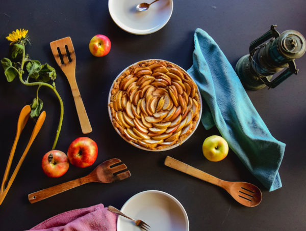 Apfelkuchen von oben fotografiert mit Küchenutensilien und Äpfeln auf dem Tisch