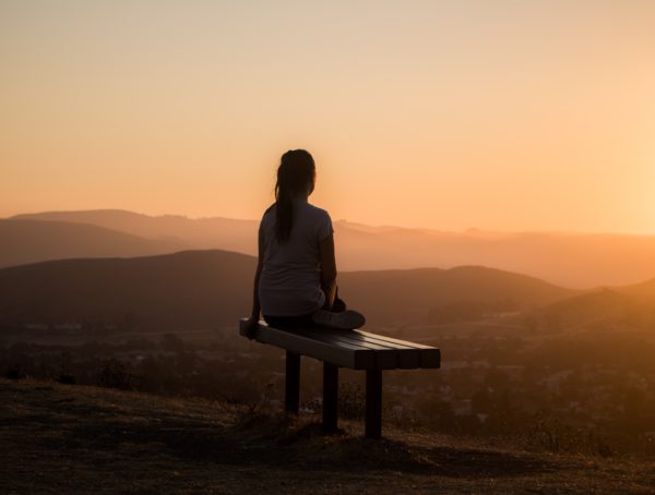 Frau sitzt bei Sonnenaufgang auf einem Berg und meditiert