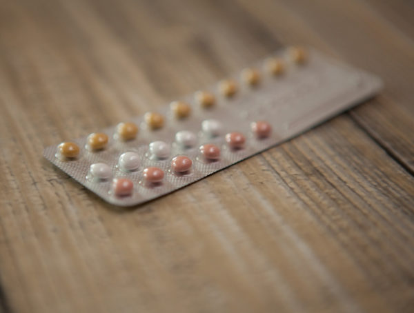 Blister einer Antibabypille mit weißen, roten und braunen Tabletten auf einem Holztisch