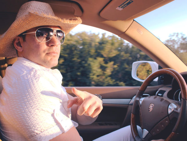 Autofahrer mit Cowboyhut und Sonnenbrille, der mit dem Zeigefinger auf den Betrachter zeigt