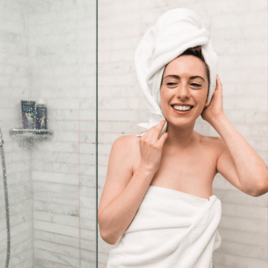Dunkelhaarige Frau tritt mit Handtuch um den Körper und um den Kopf aus einer Dusche