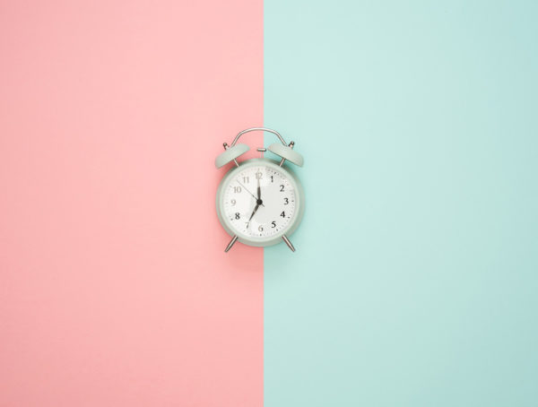 grauer Wecker vor einem rosa Hintergrund auf der linken Seite und einem Mintgrünen auf der rechten Seite