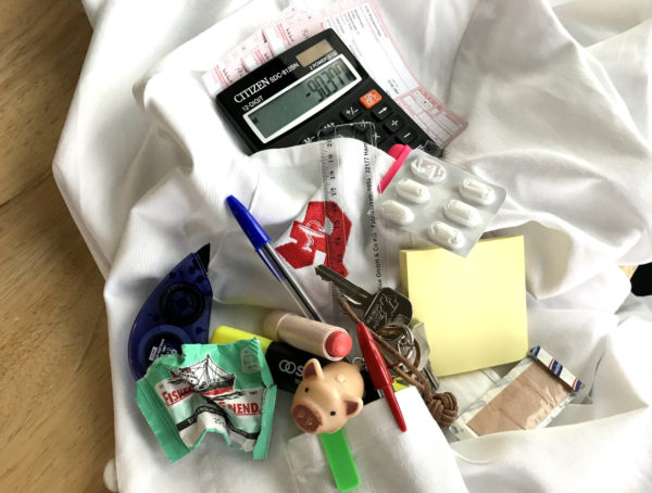 Kitteltaschenchaos mit Lineal, Rezepten, Schlüsselbund, Lippenstift, Pflaster, Post-it, Tabletten, Tipp-Ex, Stiften und Taschenrechner