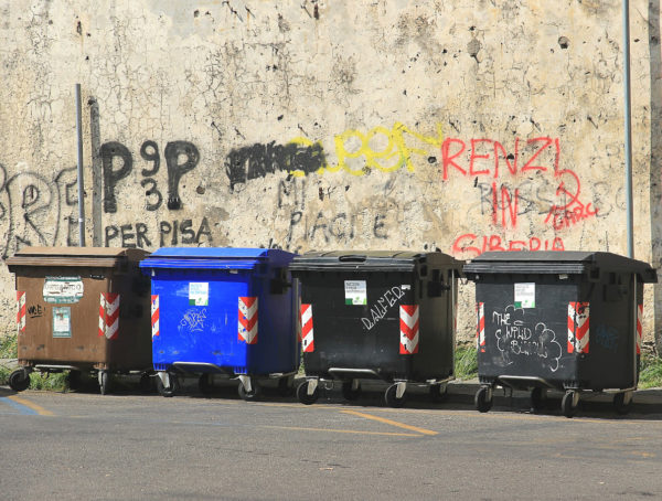 braune, blaue und zwei schwarze Müllkontainer nebeneinander vor einer Graffitiwand