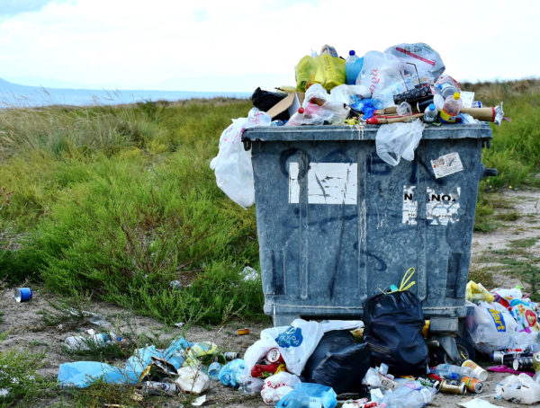 Mülltonne, die voller Plastikmüll ist. Auch davor liegen Plastiktüten herum.