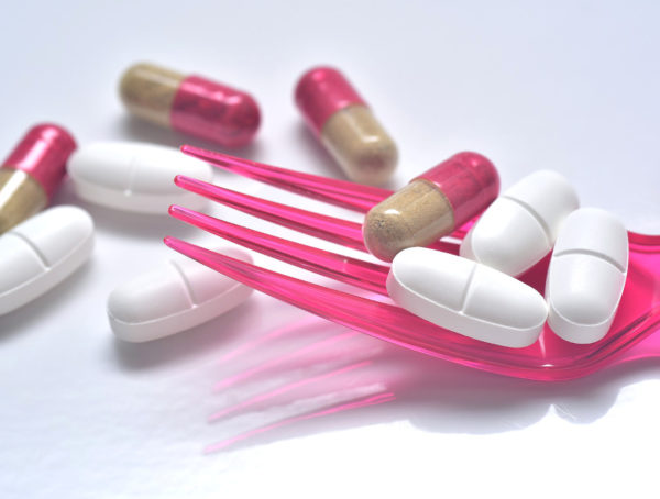 weiße Tabletten und pink-braune Kapsel auf einer pinken Plastikgabel