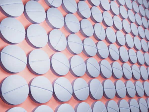 weiße Tabletten mit Bruchkerbe auf rosa Untergrund in schräger Ansicht