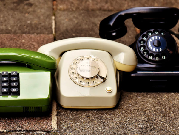 beiges und schwarzes Telefon mit Wählschiebe. Links ist ein grünes Telefon mit Tastaturfeld