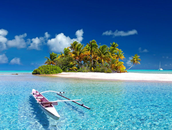 Insel mit Palmen im blauen Meer, davor liegt ein Boot