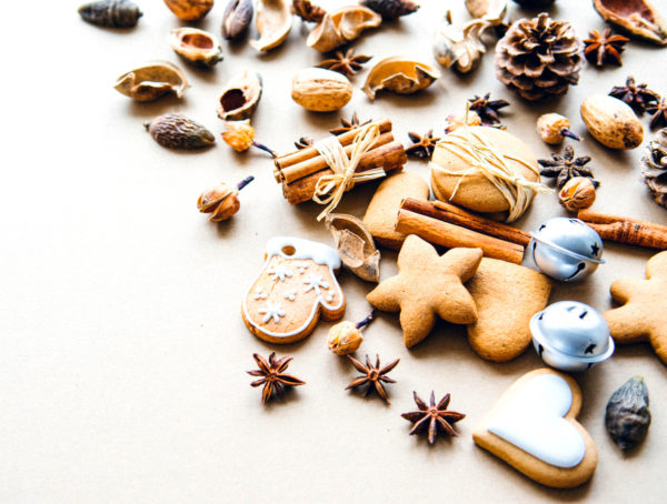 Weihnachtsplätzchen und Gewürze wie Sternanis und Zimt sowie Mandeln und Tannenzapfen auf einem Tisch