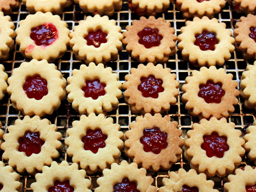 Weihnachtsplätzchen in Blumenform. In der Mitte ist ein Loch mit roter Marmelade