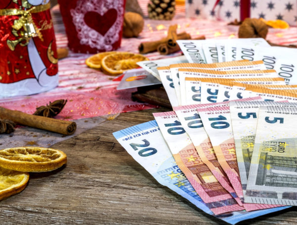 aufgefächrte Geldscheine auf einem Tisch mit Weihnachtsmann, Zimtstangen und Orangenscheiben