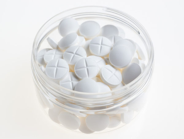 weiße runde Tabletten mit Bruchkerbe in einem Glas mit Schreaubverschluss, das offen ist