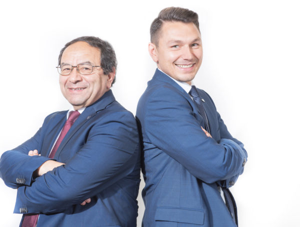 Dr. Naggar und Sohn Rücken an Rücken mit verschränkten Armen in blauem Anzug