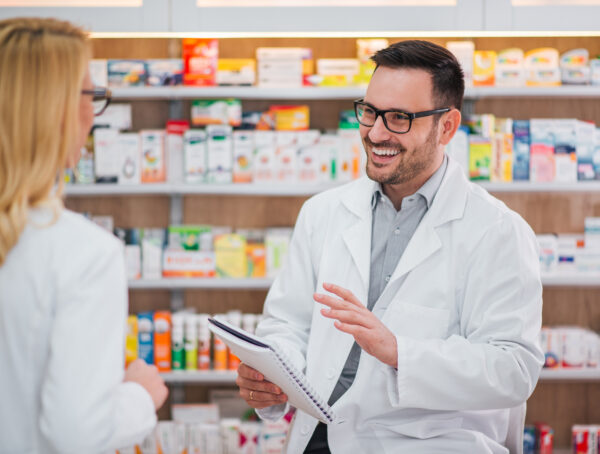 Ein lächelnder Apotheker unterhält sich mit einer Kollegin und verbreitet positive Stimmung in den Apotheke.