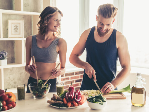 Schöne junge Sportler sprechen und lächeln, während sie zu Hause gesund kochen in der Küche