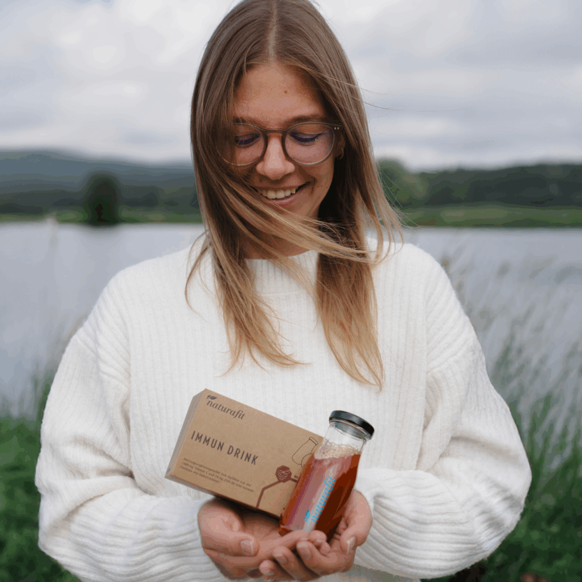 Junge Frau hält Verpackung vom naturafit Immun Drink und eine kleine Glastrinkflasche in beiden Händen