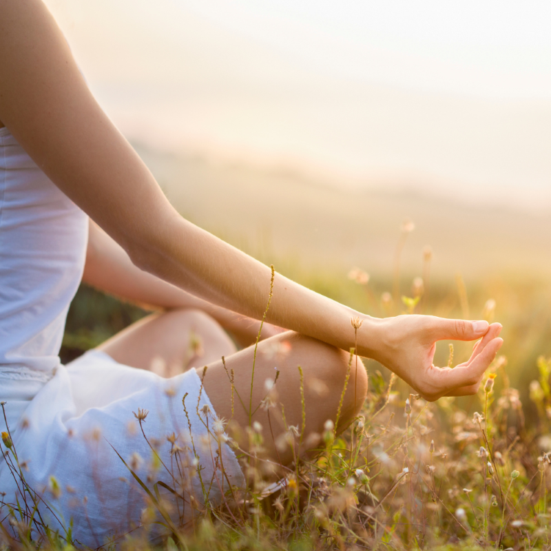Eine Person sitzt im Schneidersitz auf einer Wiese und meditiert. Die Szene ist in warmes, weiches Sonnenlicht getaucht.