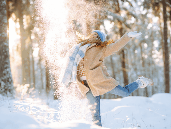 Fröhliche Person wirft im verschneiten Wald Schnee in die Luft und springt vor Wintersonne.