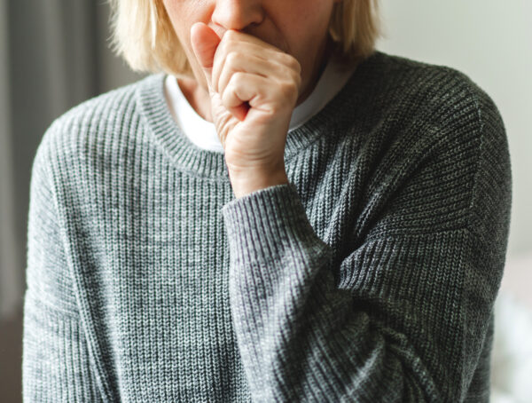 Eine ältere Frau hustet und hält sich die Hand vor den Mund.