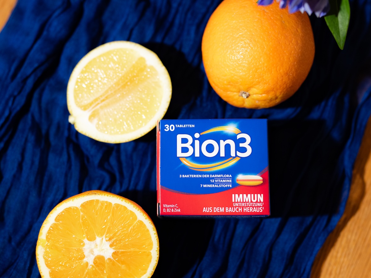 Packung Bion3 Immun* mit Zitrone und Orange auf blauem Stoff und Holzuntergrund.