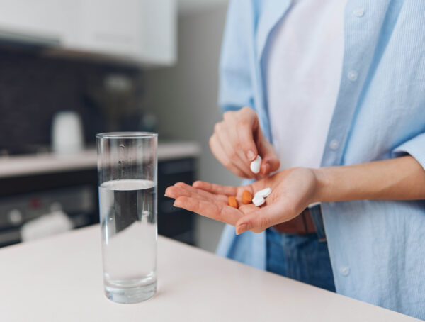 Symbolbild mit einer Frau, die in einer Hand verschiedene Tabletten hält, daneben ein Glas Wasser.