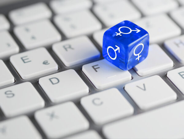 Symbolbild mit einem blauen Würfel mit verschiedenen Geschlechter-Symbolen an den Seiten, der auf einer Computer-Tastatur liegt