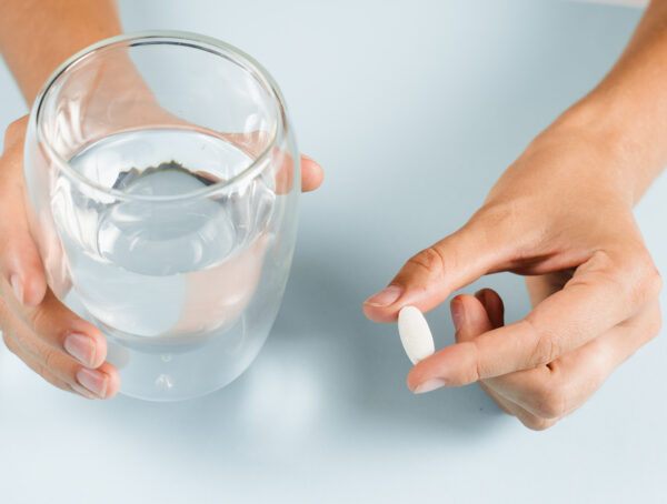 Symbolbild mit einer Hand die ein Wasserglas hält und einer mit einer Tablette.
